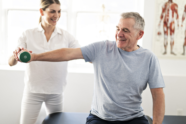 Female physical therapist assisting an older male patient with a weight-lifting exercise